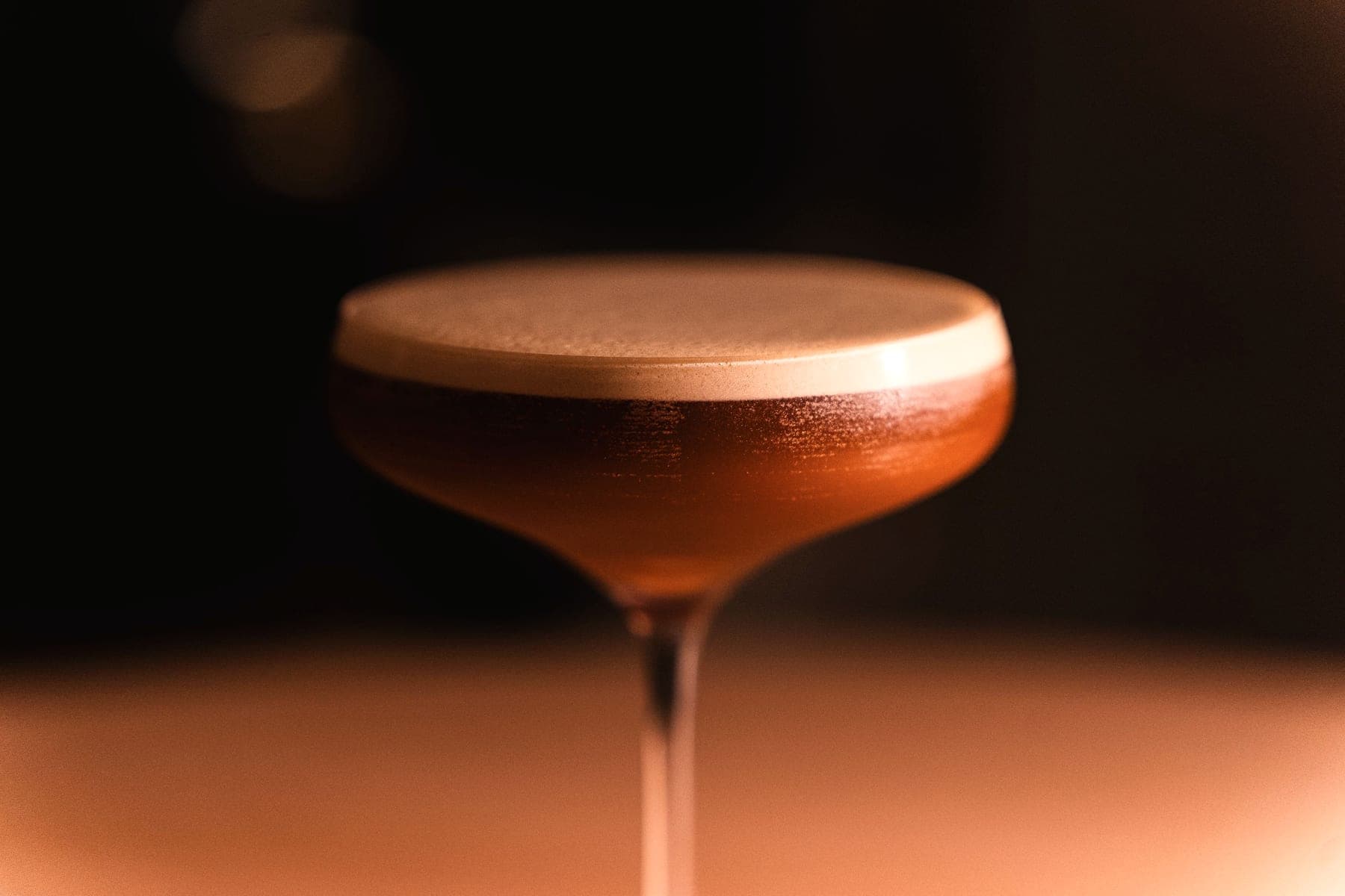 An espresso martini in a coupe, glowing in low bar light.
