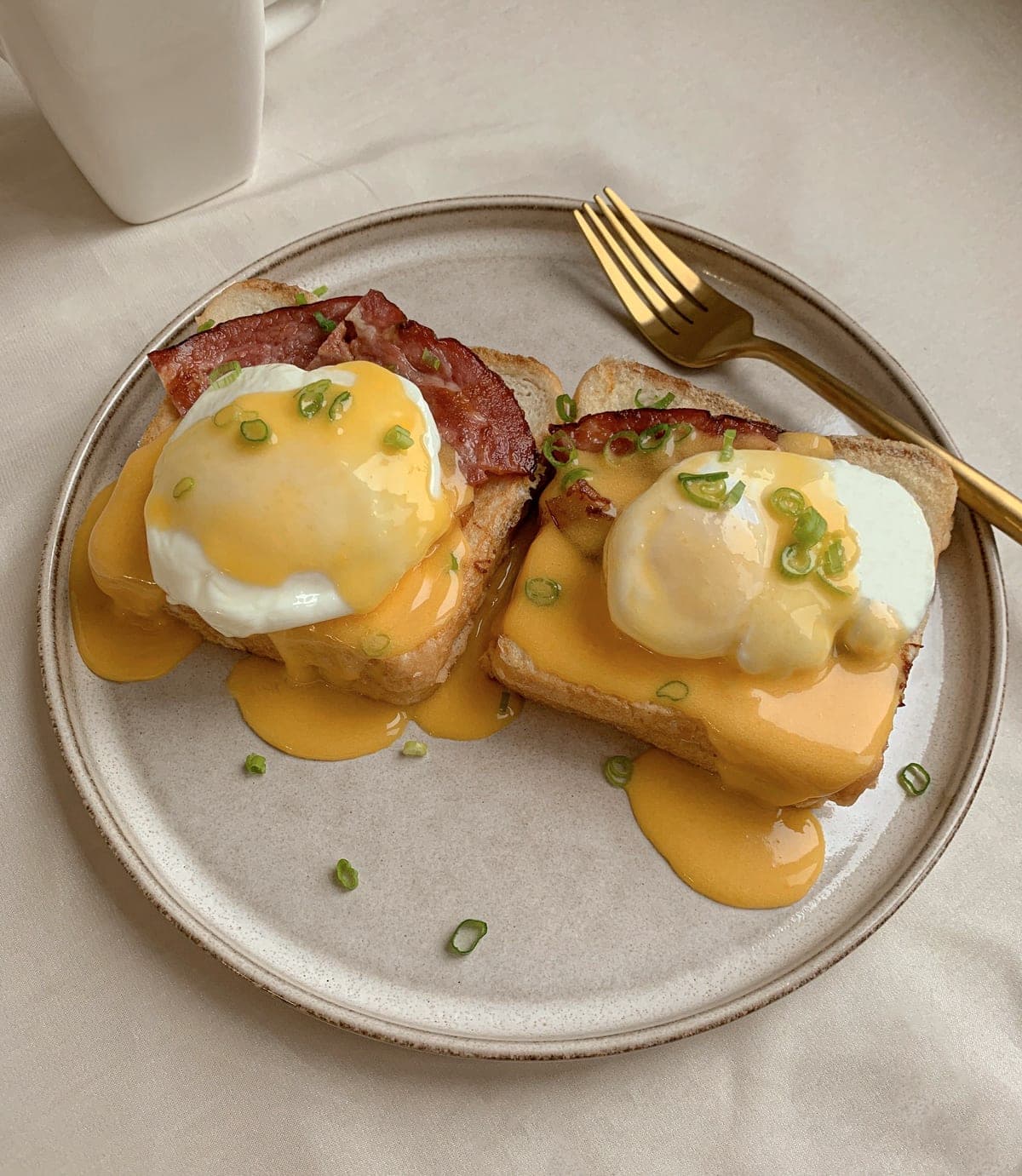 Eggs Benedict: poached eggs and hollandaise over seared beef bacon on thick toast, scattered with chives.