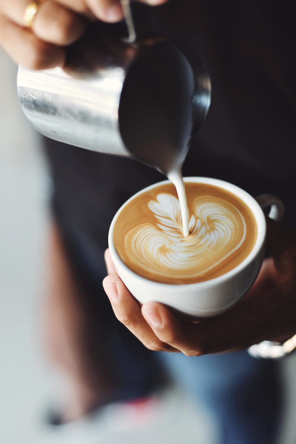 A barista pours steamed milk into a white cup, drawing latte art.