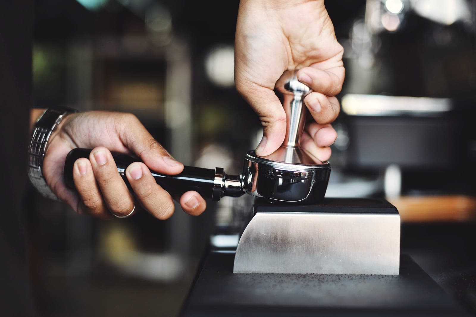 A barista's hands tamping ground coffee into a portafilter.