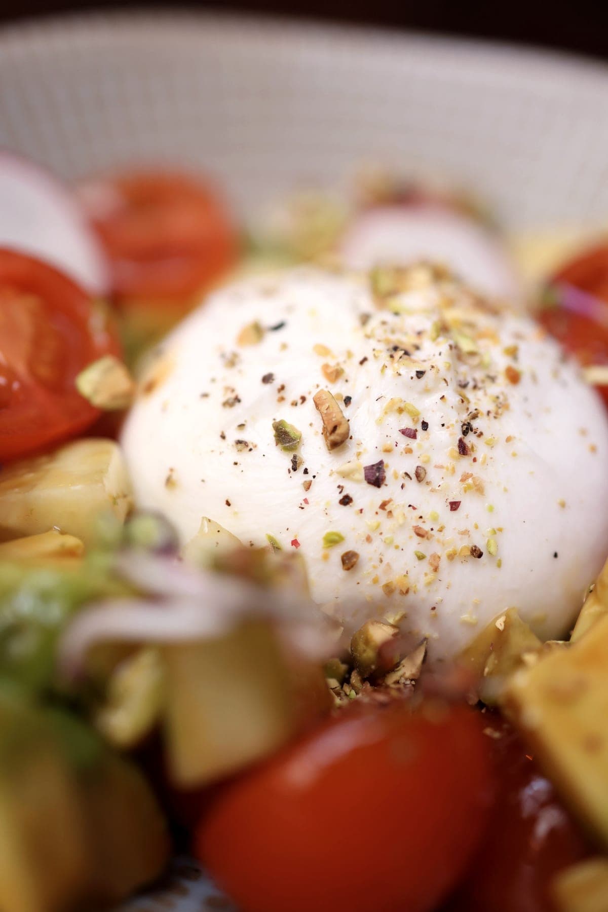 A whole burrata scattered with crushed pistachio, among cherry tomatoes.