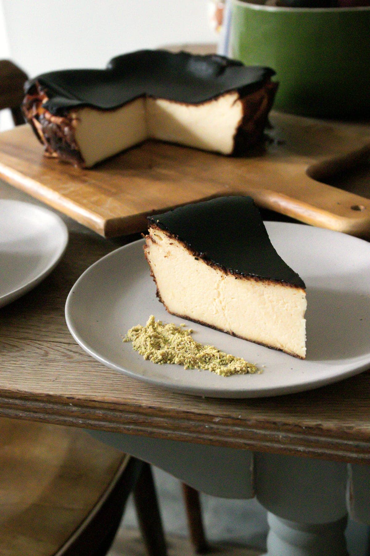 A slice of Basque cheesecake with a burnt top and soft centre, the rest of the cake on a board behind.