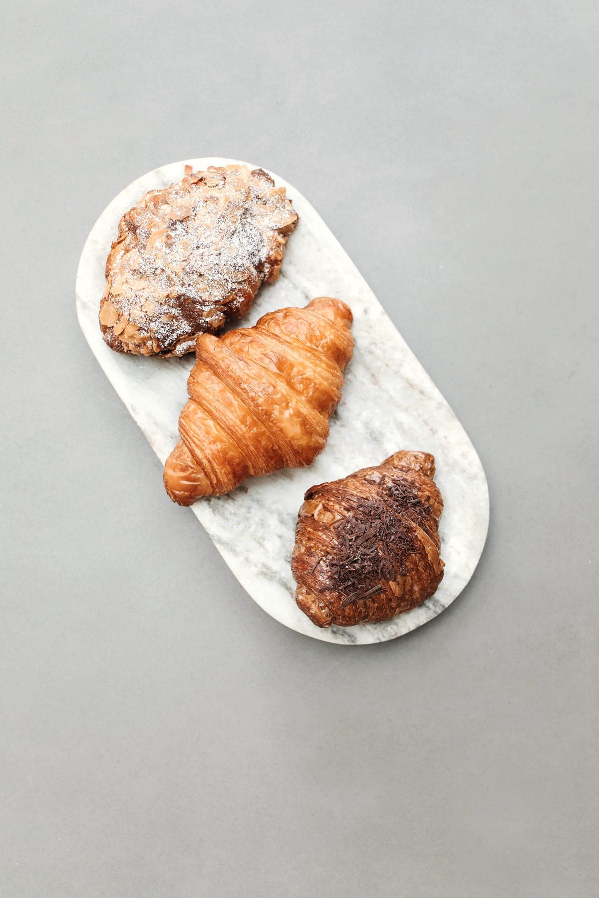 An almond croissant, a butter croissant and a chocolate pastry on a marble board.