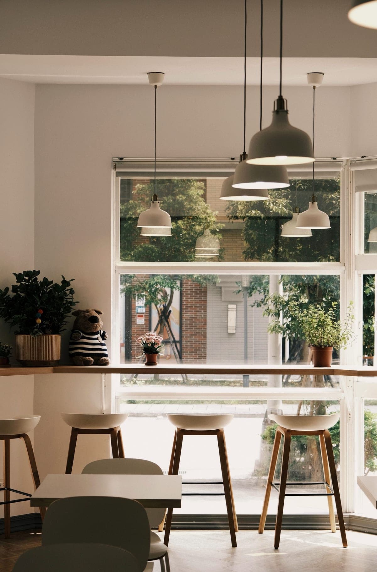 A bright café room with pendant lamps, high stools and tall windows onto greenery.