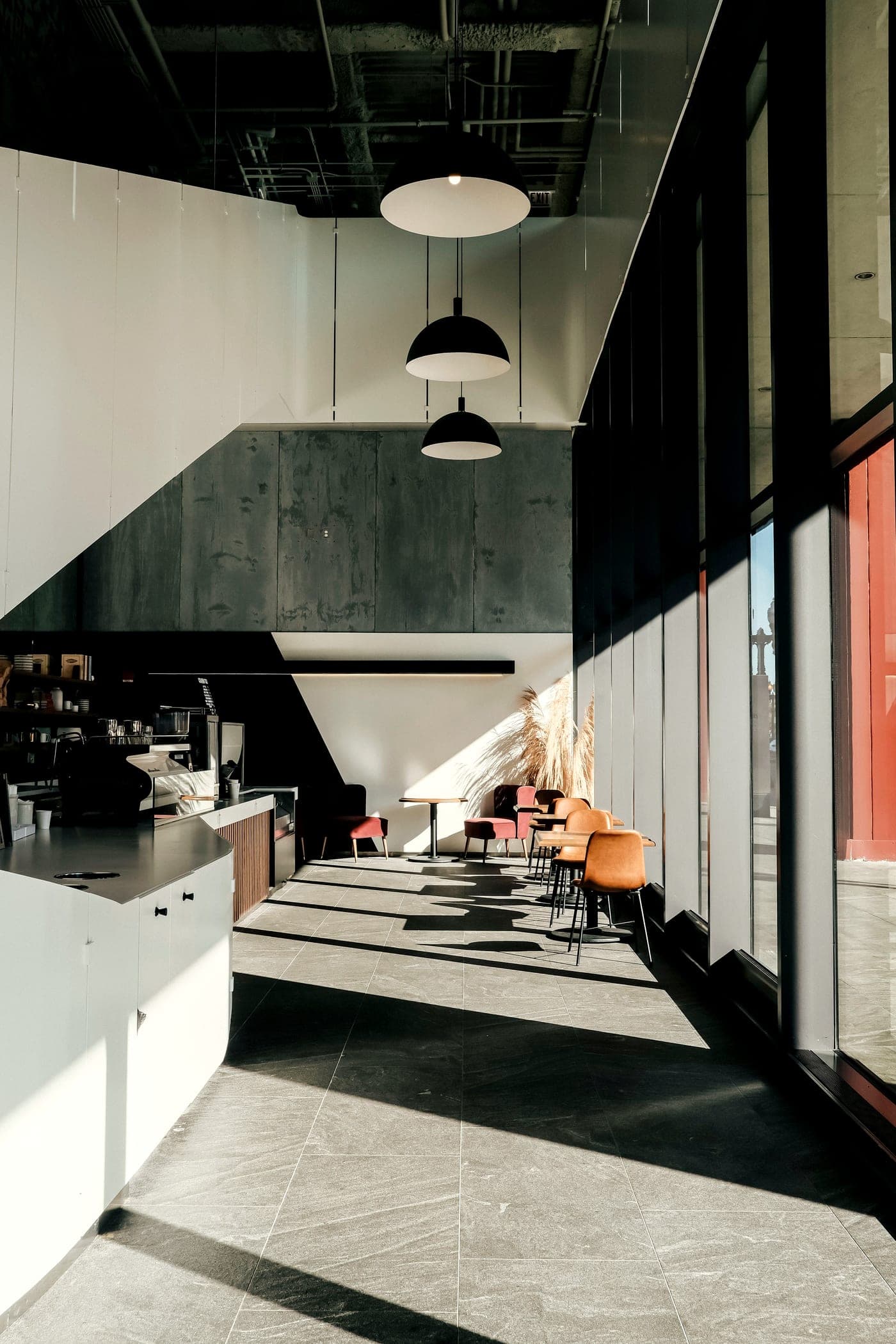 Morning sun cuts long shadows across a pale stone floor and a long counter in a modern café.